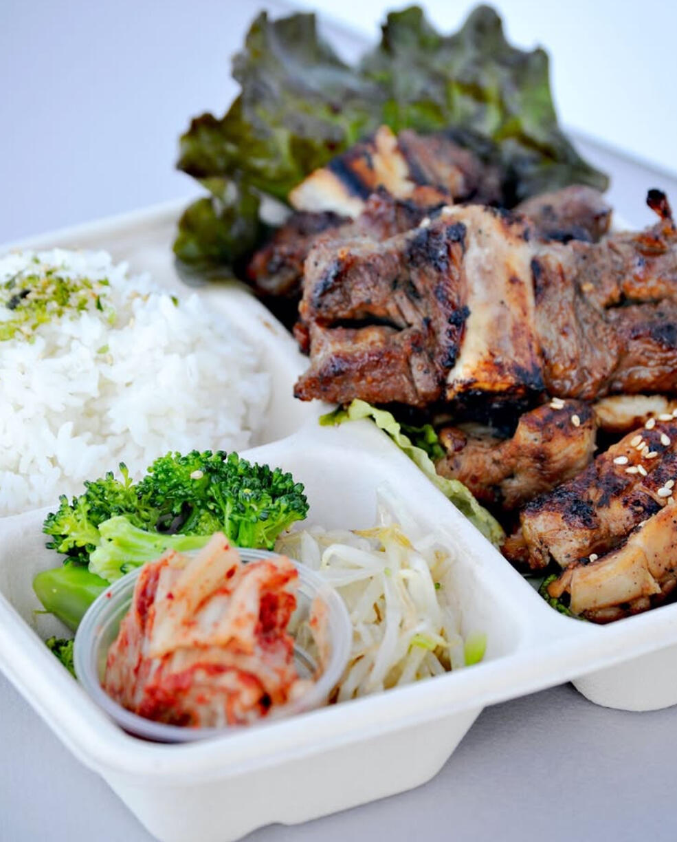 Korean Lunch Box with Grilled Galbi, Kimchi, and Rice – Authentic Local Meal A takeout Korean lunch box featuring grilled galbi (marinated short ribs), steamed rice, kimchi, broccoli, and bean sprouts, presented with fresh lettuce.
