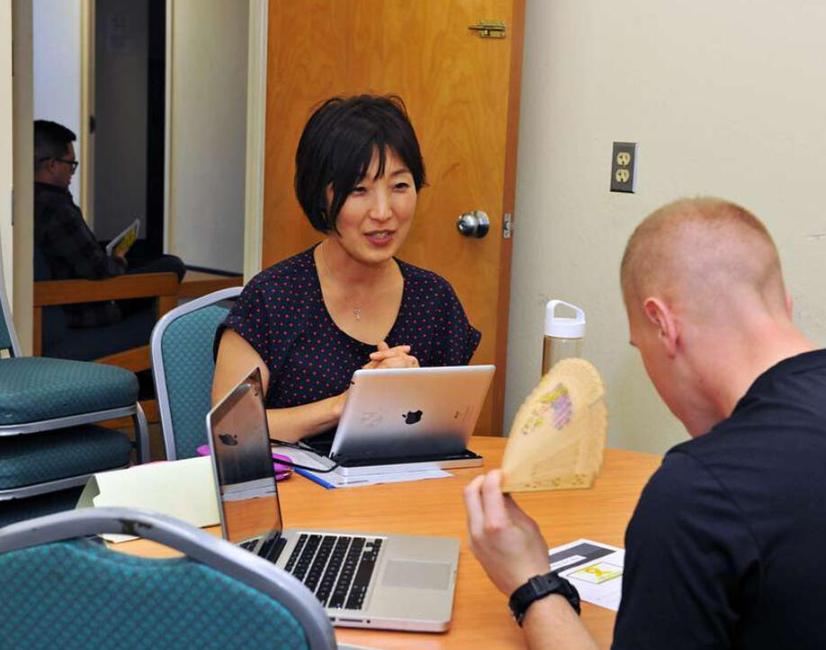 Korean Language Class for Foreigners – One-on-One Learning Session in Korea A Korean language teacher engages in a one-on-one lesson with a foreign student, using laptops and traditional Korean fan materials to support interactive learning.